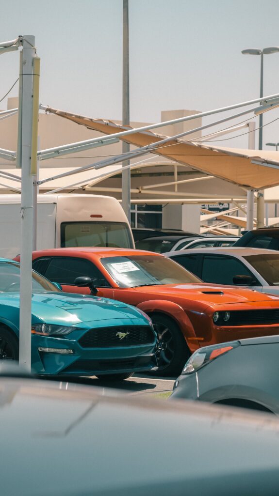 Brightly colored muscle cars in a car dealership parking lot showcasing urban automotive appeal.
